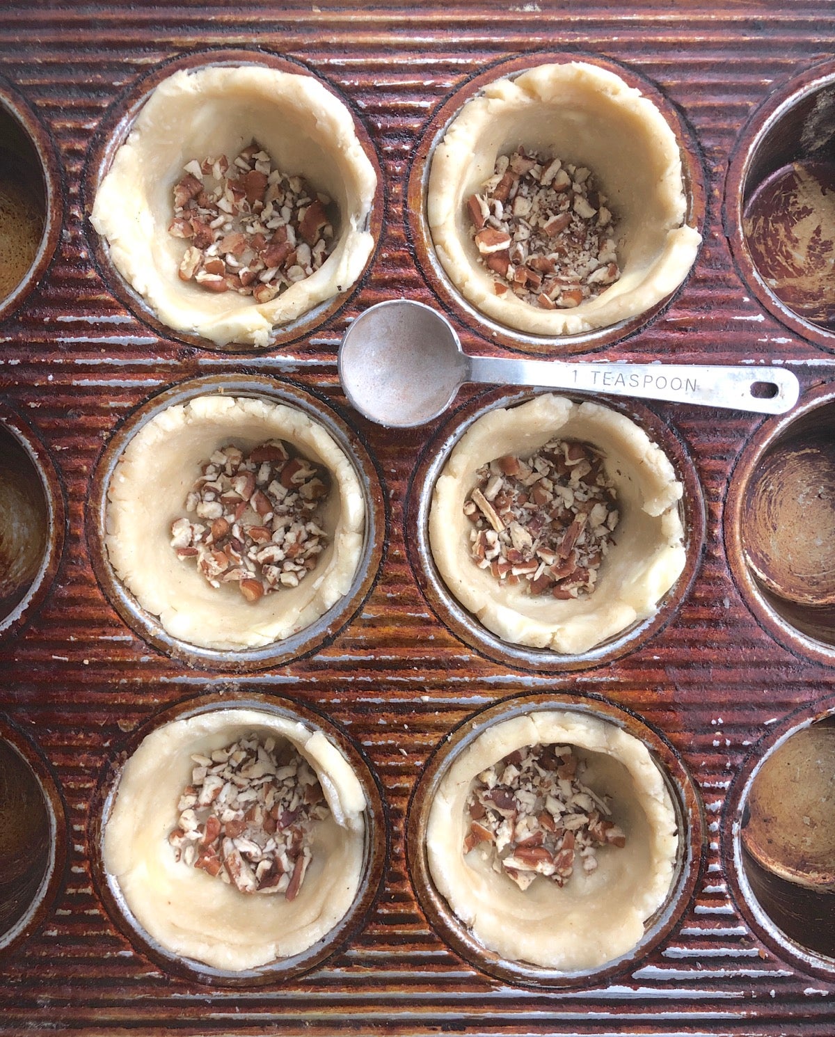 Mini pie crusts for pecan pie with diced pecans sprinkled into the bottom.